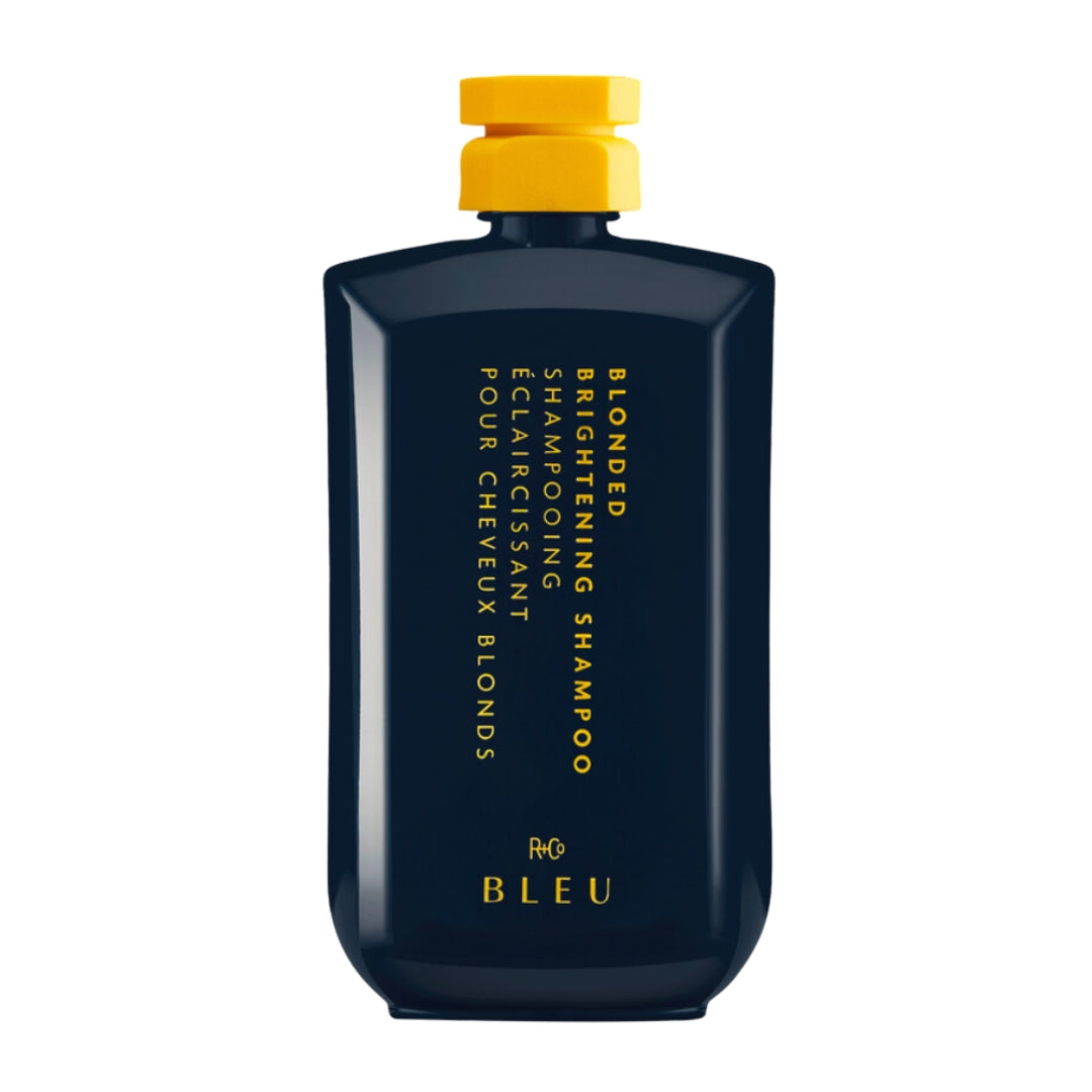 A navy bottle of Blonded Brightening Shampoo by R+Co with a yellow cap, labeled with yellow text, against a white background.