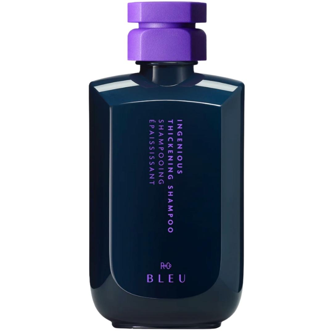 A bottle of R+Co Blue brand Ingenious thickening shampoo with a purple cap, labeled for strengthening hair, clarifying, and adding shine.