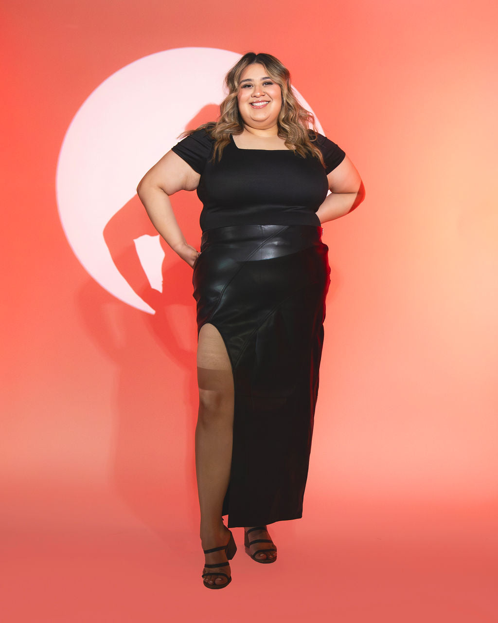 Jackie standing in spotlight wearing black outfit against orange background
