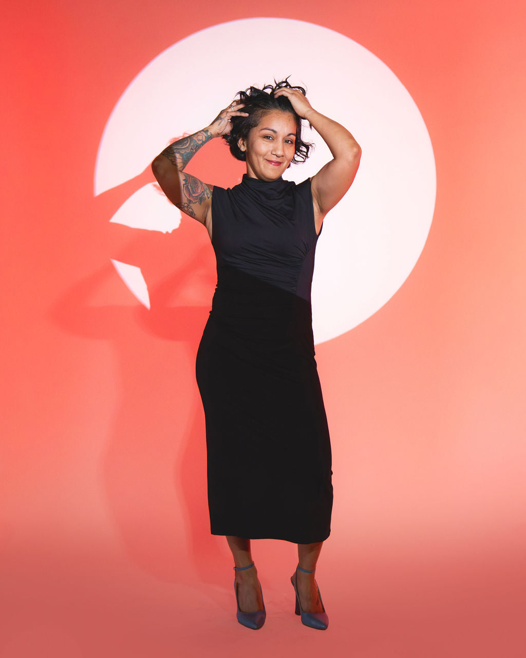Nana standing in spotlight wearing black dress against orange background