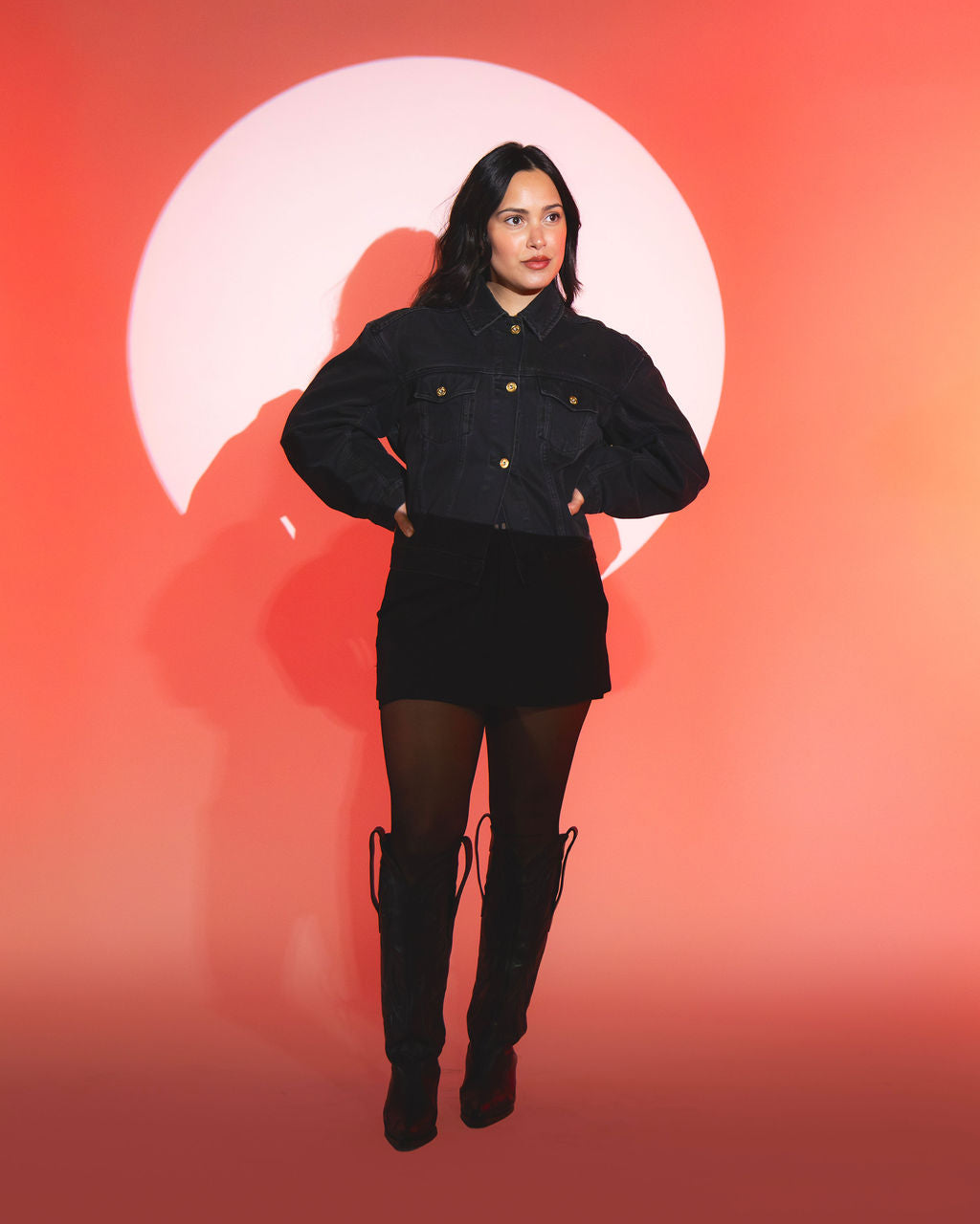 Sofie standing in spotlight wearing black outfit against orange background