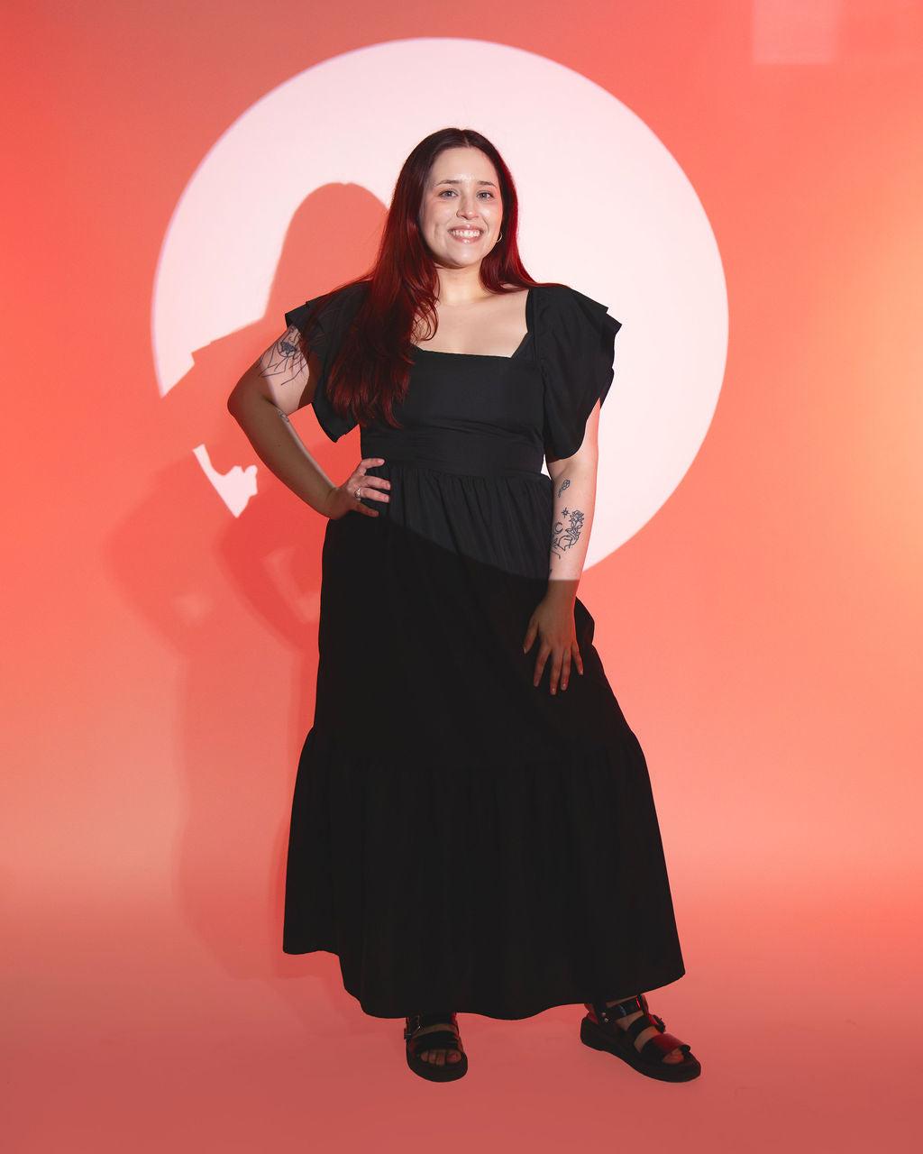 X standing in spotlight wearing black dress against orange background