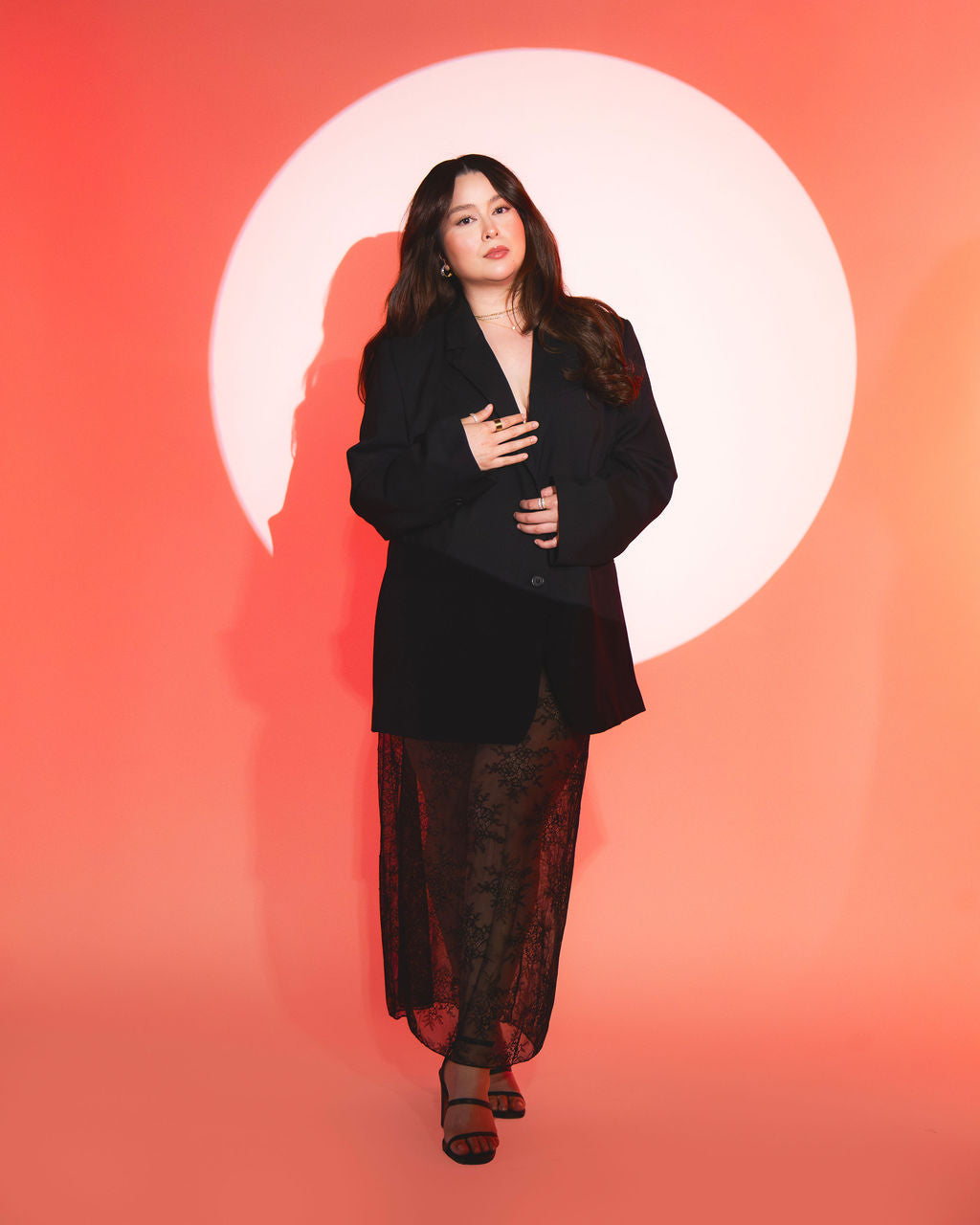 Xochil standing in spotlight wearing black outfit against orange background