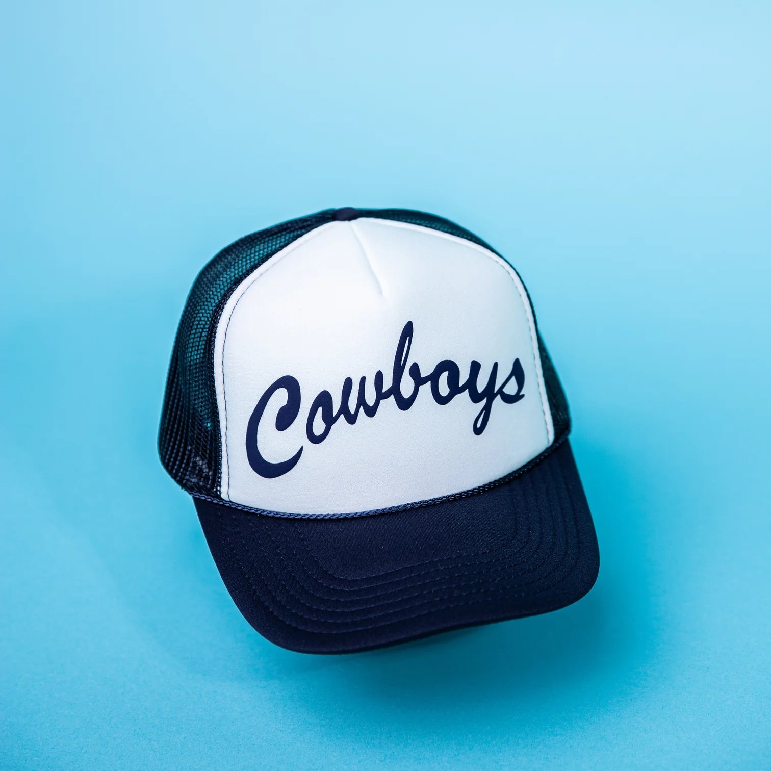 A trucker hat with the word 'Cowboys' written across the front in blue lettering on a white background