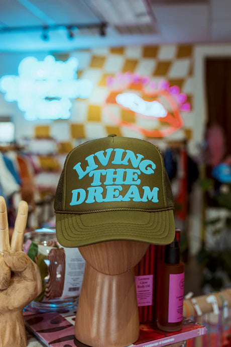 A trucker hat displayed on a mannequin head, with the text 'LIVING THE DREAM' written on it.