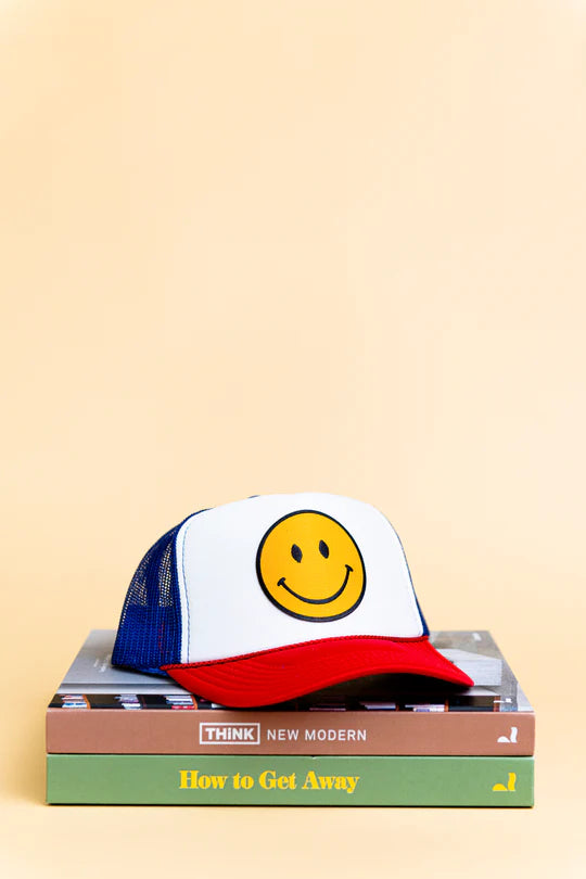Colorful trucker hat with smiley face design on a stack of books with a beige background