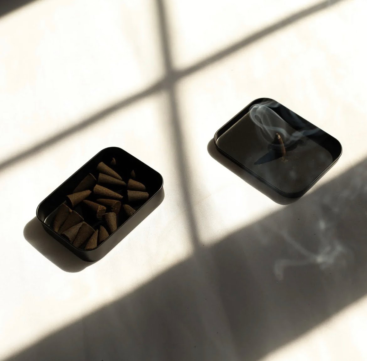 An open black tin of Dilo brand incense cones. The lid holds one cone which is smoking.