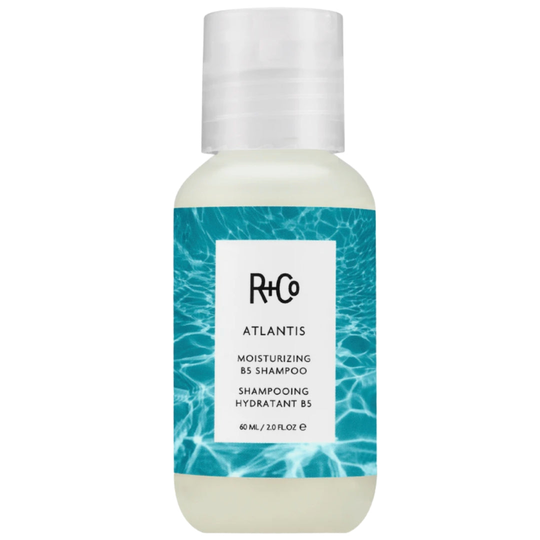 A travel-sized bottle of R+Co Atlantis Moisturizing Shampoo with a white dispenser cap and a label featuring a blue aquatic scene with ripples, indicating a moisturizing effect.