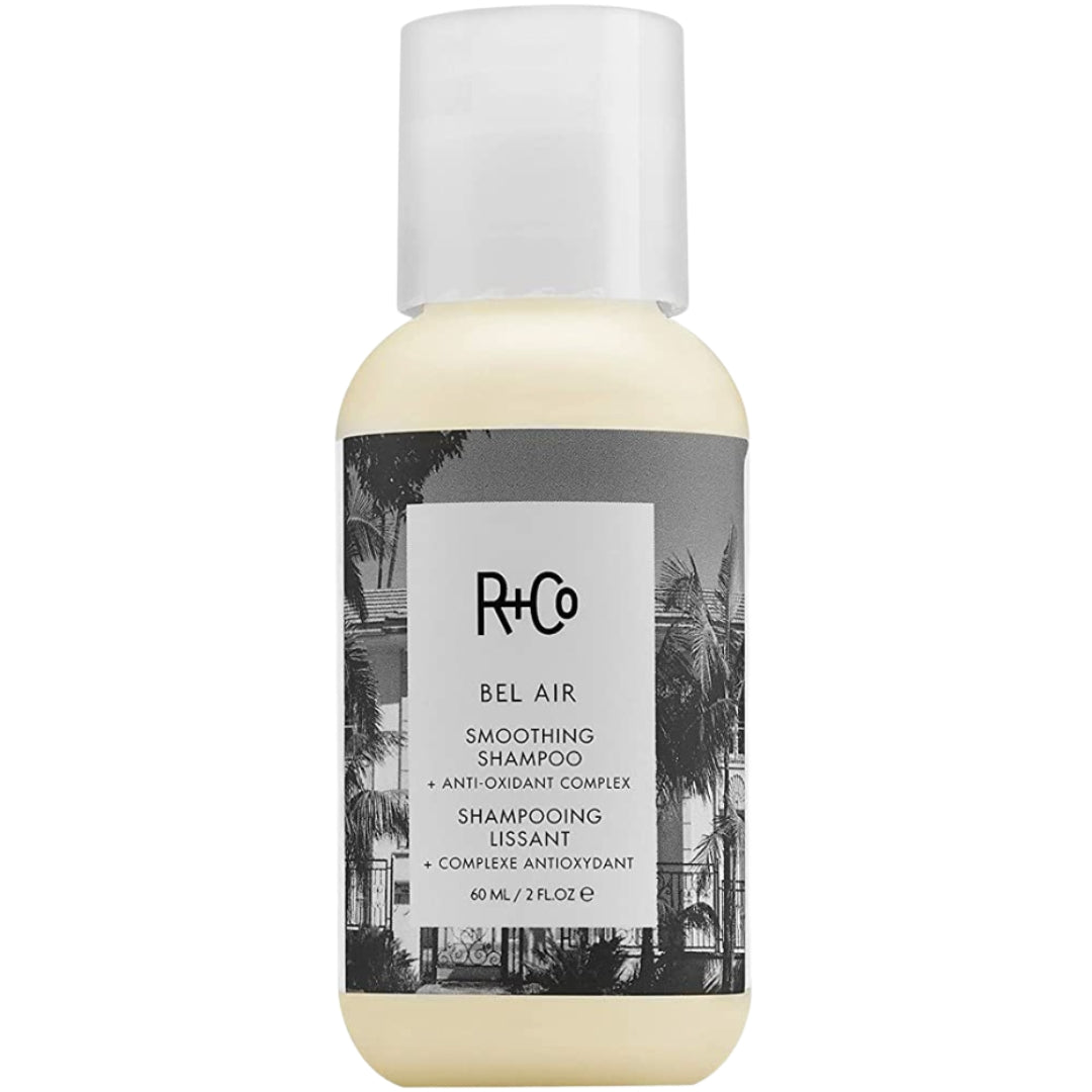 A travel-sized bottle of R+Co Bel Air Smoothing Shampoo with a label featuring a black and white photograph of a palm tree and building.