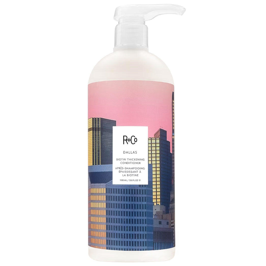A bottle of Dallas Biotin Thickening Conditioner by R+Co, featuring a cityscape of Dallas on the label.