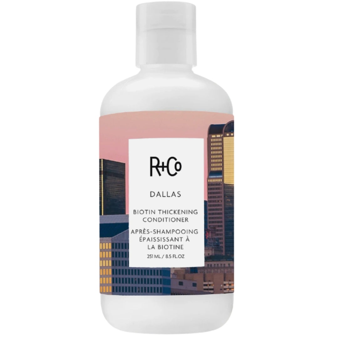 A bottle of Dallas Biotin Thickening Conditioner by R+Co, featuring a cityscape of Dallas on the label.