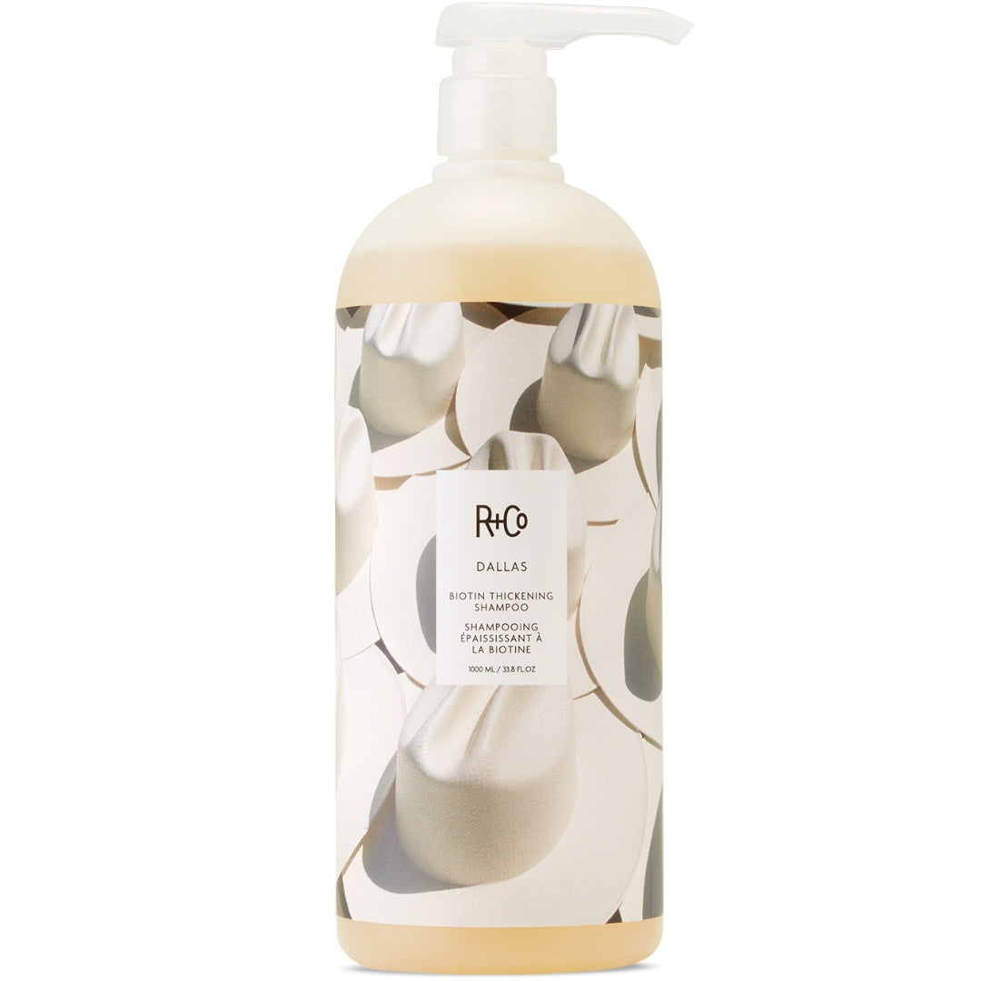 A bottle of R+Co Dallas Biotin Thickening Shampoo with a label featuring a black and white cowboy hat pattern.