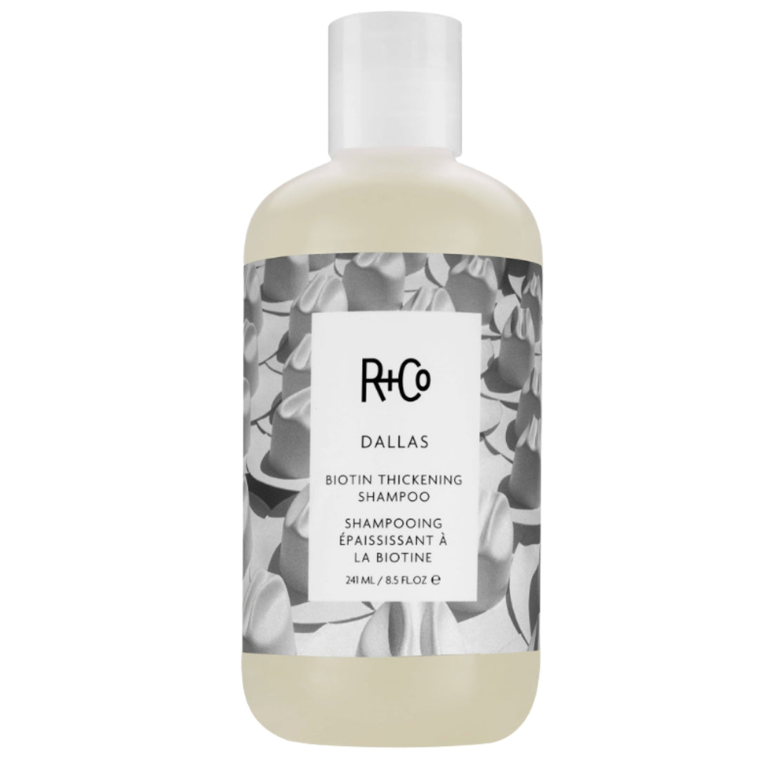 A bottle of R+Co Dallas Biotin Thickening Shampoo with a label featuring a black and white cowboy hat pattern.