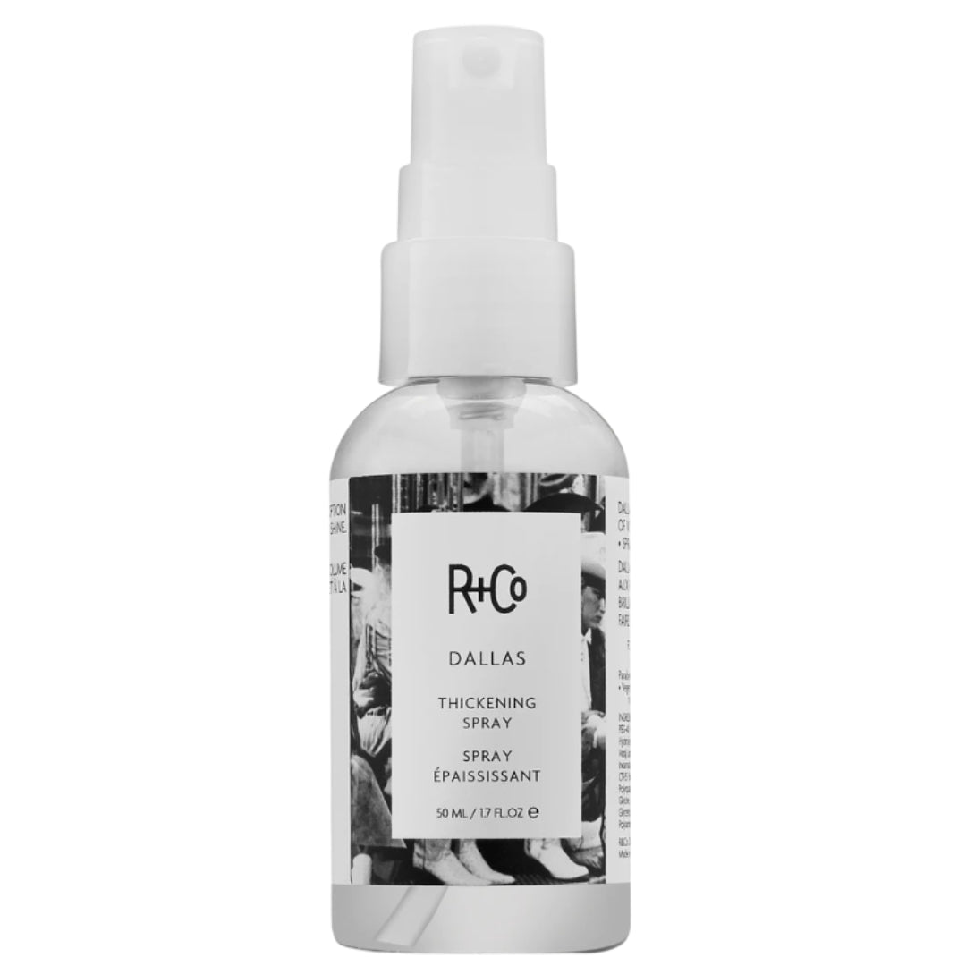 A spray bottle of R+Co DALLAS thickening spray with a label featuring a black and white cowgirls image