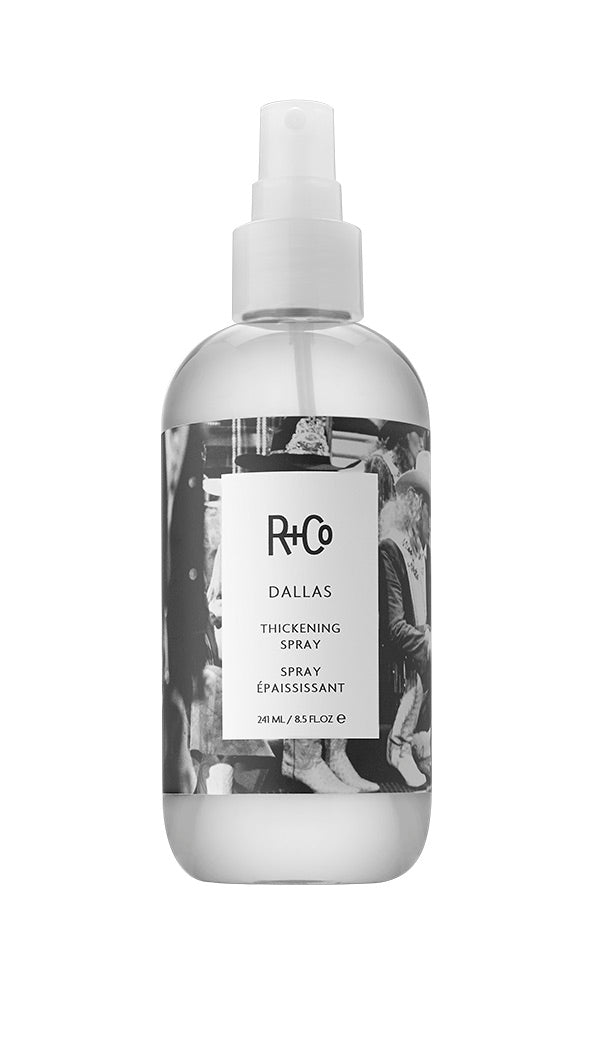 A spray bottle of R+Co DALLAS thickening spray with a label featuring a black and white cowgirls image