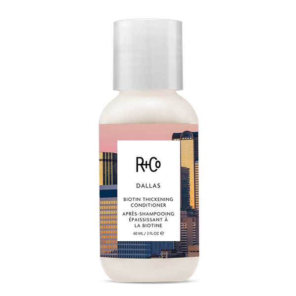 A travel-sized bottle of R+Co Dallas Biotin Thickening Conditioner with a label featuring Dallas cityscape.