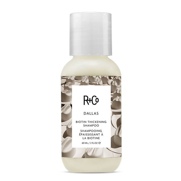 A travel-sized bottle of Dallas Biotin Thickening Shampoo by R+Co with a white label and cowboy hat pattern.